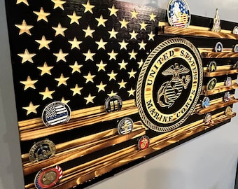 May include: A wooden American flag with a black background and gold stars. The flag has a shelf for displaying challenge coins. The shelf is decorated with a gold United States Marine Corps emblem.