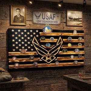 May include: A wooden wall-mounted display rack featuring a charred American flag design with horizontal shelves for challenge coins. The center displays a large gold-toned United States Air Force emblem, with additional coins arranged on the shelves.