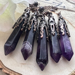 May include: Five amethyst crystal point pendants with ornate silver and copper filigree settings. The pendants are hanging from a chain.