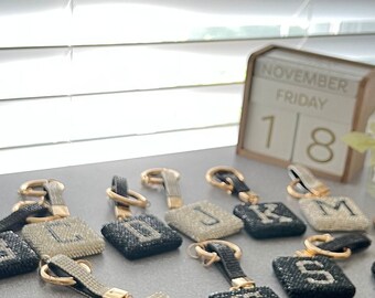 May include: A collection of 18 black and white rhinestone letter keychains with gold rings. The keychains are arranged in a semi-circle on a white surface. The letters are A, B, C, D, J, K, L, M, N, P, S, T, and Z.
