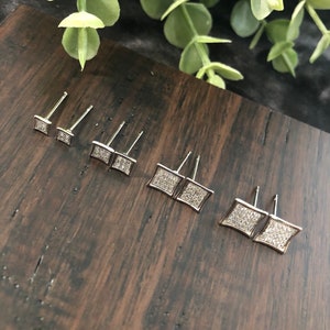 May include: Set of six silver square stud earrings with clear cubic zirconia stones. The earrings are arranged in order of size, with the smallest on the left and the largest on the right.