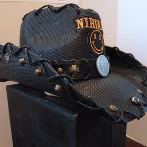 May include: Black cowboy hat with a black and gold band, a silver coin, and a patch that says "NIRVANA" with a smiley face.