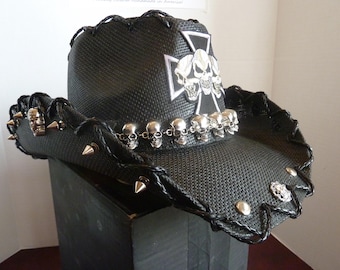May include: Black cowboy hat with silver skull accents, spikes, and a cross design. The hat features a woven texture and a decorative band of small skulls around the brim. A unique accessory for a bold look.