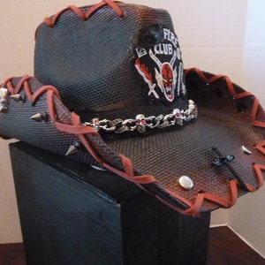 May include: A black cowboy hat with red stitching and a skull and crossbones design. The hat has a silver chain with skull charms and a patch that says "Fire Club".