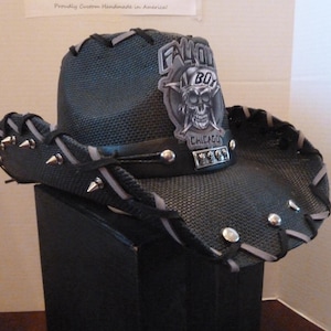 Peut inclure: Chapeau de cowboy noir avec un écusson de crâne et d'os croisés qui dit "Fallout Boy Chicago". Le chapeau est orné de clous argentés et d'une bordure grise.