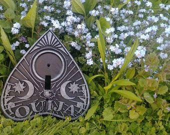 May include: A silver and black Ouija board with a crescent moon and star design. The board is surrounded by blue forget-me-not flowers.