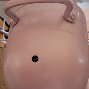 Puede incluir: Un ventilador el&eacute;ctrico de estilo vintage en un tono rosa suave. El ventilador presenta un cuerpo redondeado con un asa, una jaula protectora y aspas blancas. El dise&ntilde;o evoca una est&eacute;tica retro, adecuada para la decoraci&oacute;n del hogar.