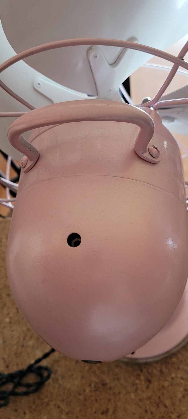 Puede incluir: Un ventilador el&eacute;ctrico de estilo vintage en un tono rosa suave. El ventilador presenta un cuerpo redondeado con un asa, una jaula protectora y aspas blancas. El dise&ntilde;o evoca una est&eacute;tica retro, adecuada para la decoraci&oacute;n del hogar.