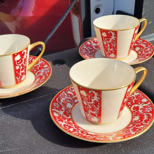 May include: Three vintage teacups and saucers. The cups are cream-colored with a red floral design and gold trim. The saucers have a matching red floral pattern. The cups have gold handles.