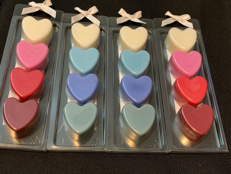May include: Four sets of heart-shaped wax melts in various colors, including white, pink, red, blue, and purple. Each set is packaged in a clear plastic container with a white ribbon.