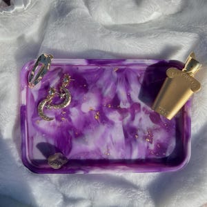 May include: Purple and white resin tray with gold flecks. The tray has a marbled design and is decorated with gold stars and moons. A gold bottle of perfume is on the tray.