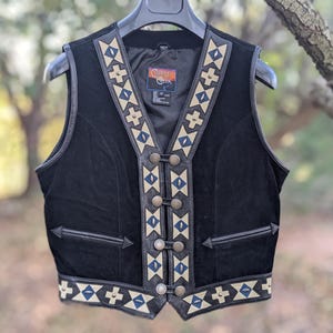 May include: Black suede vest with a geometric pattern in white and blue. The vest has a zipper closure and a label that reads "Cutter & Buck".