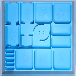 May include: A light blue organizer with multiple compartments for storing small items. The compartments have various shapes and sizes, including circles, squares, and rectangles. The organizer is made of plastic and has a smooth surface.