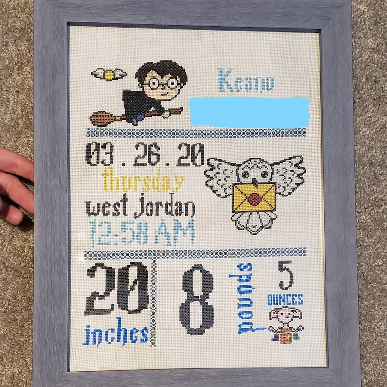 May include: A white cross-stitch with a Harry Potter theme. It features a baby's birth details, including the date, time, and weight. The baby's name is Keanu. The cross-stitch also includes a picture of Harry Potter flying on a broomstick, a snowy owl, and a Dobby.