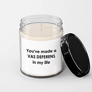May include: A clear glass candle jar with a black lid. The candle is white and has a label that reads "You've made a VAS DEFERENS in my life".