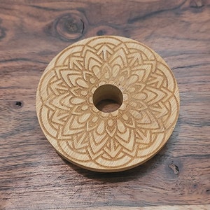 May include: A round wooden coaster with a laser-etched mandala design. The coaster has a hole in the center.