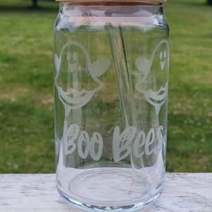 May include: A clear glass jar with a bamboo lid and a glass straw. The jar has a ghost design and the text "BOO BEES" etched on the side.