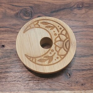 May include: A wooden coaster with a crescent moon design carved into the surface. The moon is decorated with intricate floral patterns.