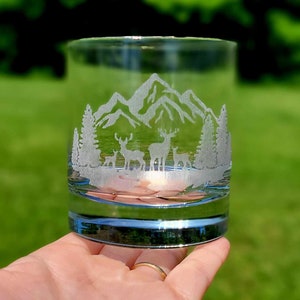 May include: A clear glass tumbler with an etched design of mountains and deer. The design is in white and is visible against the clear glass.