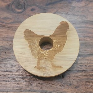 May include: A round, wooden coaster with a laser-etched design of a chicken. The coaster has a hole in the center for a beverage.