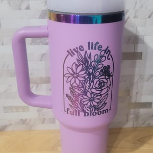 May include: A lavender travel mug with a black and white floral design and the text "live life in full bloom".