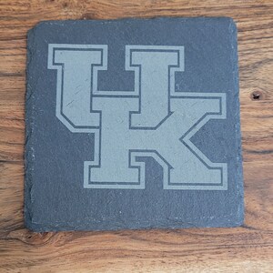 May include: A black slate coaster with a gray "UK" logo in a collegiate font.