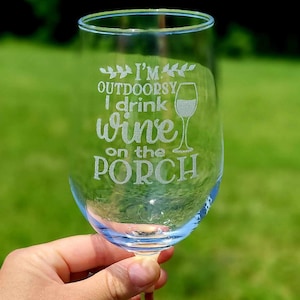 May include: A clear glass wine glass with the text "I'm Outdoorsy I drink wine on the porch" etched into the side.