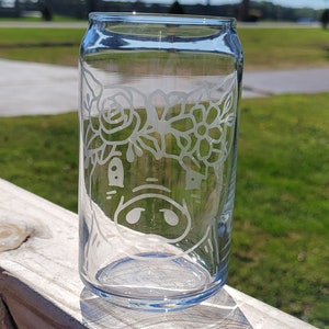 May include: A clear glass can with a floral design etched into the side. The design features a pig wearing a flower crown.