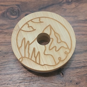 May include: A round, wooden lid with a mountain design engraved on the top. The lid has a hole in the center.