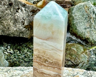 May include: A light green and brown layered crystal tower with a pointed top. The tower is sitting on a gray rock.