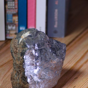 Puede incluir: Una roca grande de forma irregular con una superficie metálica gris plateada. La roca tiene una superficie rugosa y texturizada y parece estar hecha de un material denso.
