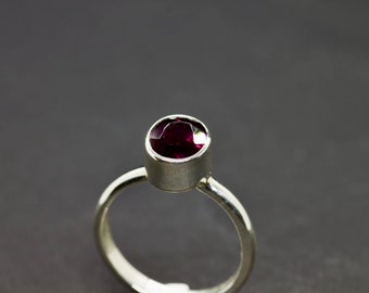 May include: A silver ring with a deep purple gemstone set in a bezel setting.