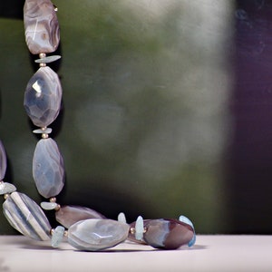 May include: A necklace made of light blue and gray agate beads with silver accents.