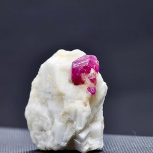 May include: A small, bright pink ruby crystal embedded in a white, rough, rock-like matrix.