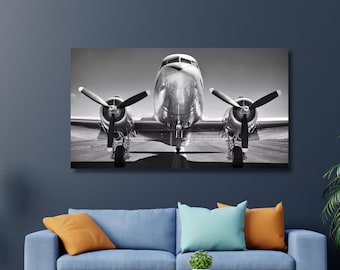 May include: A black and white photograph of a vintage airplane on a runway. The airplane is facing the camera with its propellers visible. The image is in a rectangular frame.