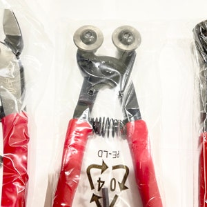May include: A pair of red-handled wire cutters with a spring mechanism and a black metal blade. The cutters are packaged in a clear plastic bag with a recycling symbol that reads "04 PE-LD".