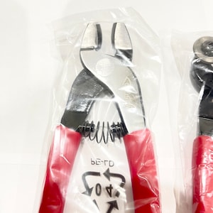 May include: A pair of red-handled wire cutters in a clear plastic bag. The cutters have a spring-loaded handle and a black metal head. The bag has a recycling symbol with the text "PE-TD 04".