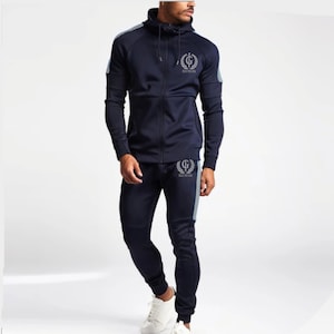May include: A navy blue tracksuit with a zippered hoodie. The hoodie has a silver logo with the text "Rise To The Gym". The tracksuit has white and blue stripes on the sides.