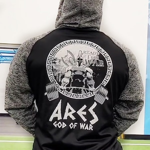 May include: Black and gray hooded sweatshirt with a white graphic of a muscular figure lifting weights. The graphic is inside a circle with a Greek key border and the text "Ready for War". Below the graphic is the text "Ares God of War".
