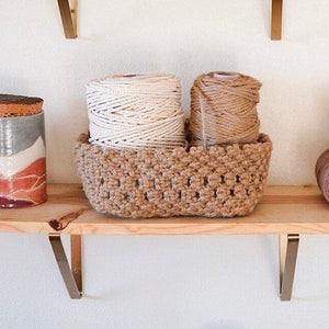 Peut inclure: Un panier en crochet marron avec deux bobines de ficelle, une blanche et une marron, posées sur une étagère en bois.