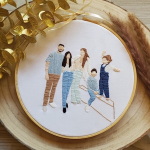 Pode incluir: Arte de bordado em aro que representa uma família de cinco pessoas. O aro é branco com uma moldura dourada. A família é bordada em vários tons de azul, marrom e branco.