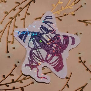 May include: A holographic sticker in the shape of a star with a purple and pink design of intertwined lines and hearts.