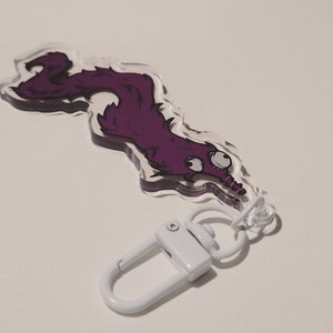May include: Purple cartoon worm keychain with large eyes and a white metal clasp.