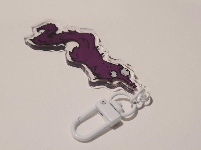 May include: Purple cartoon worm keychain with large eyes and a white metal clasp.
