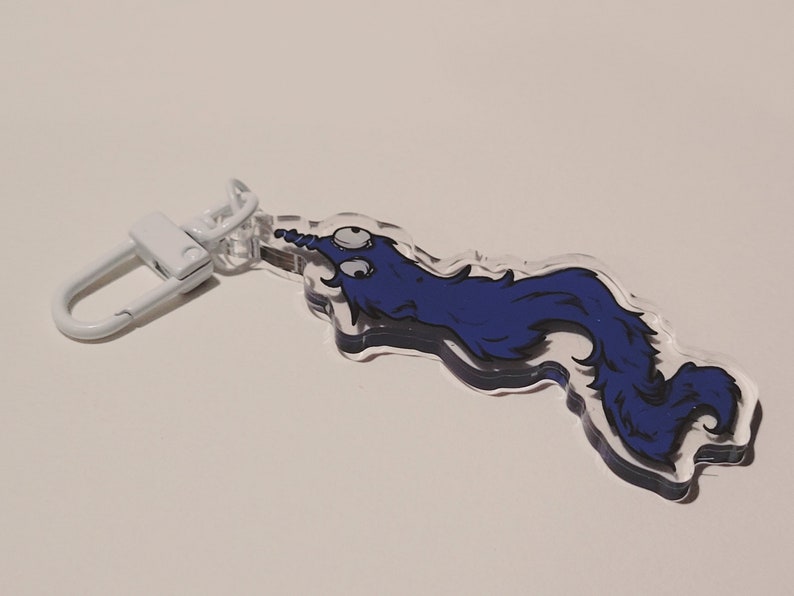 May include: A blue and white cartoon worm keychain with a white metal clasp. The worm has two large eyes and a curled tail.