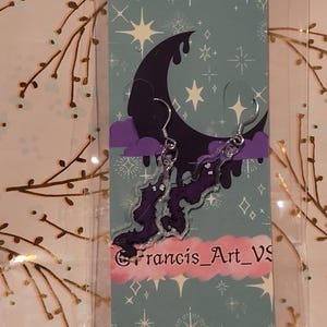 May include: Purple and black acrylic earrings featuring a crescent moon and a cloud with a purple dragon design. The earrings are on a card with a blue background and white stars. The card also has the text "@francis_art_vs".