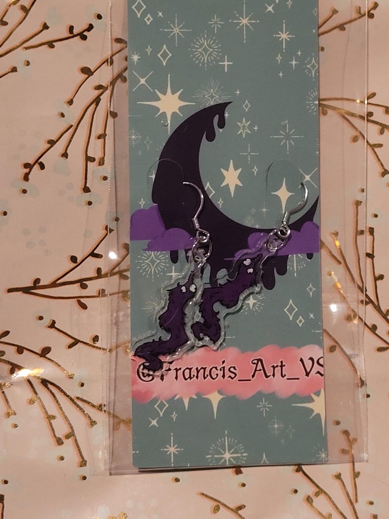 May include: Purple and black acrylic earrings featuring a crescent moon and a cloud with a purple dragon design. The earrings are on a card with a blue background and white stars. The card also has the text "@francis_art_vs".