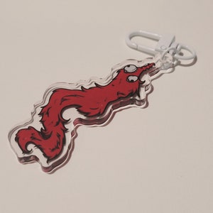 May include: A red worm-like creature with two eyes is printed on a clear acrylic keychain. The keychain has a white metal ring and clasp.