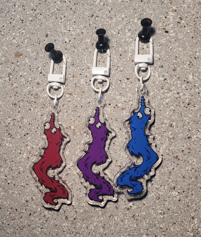 May include: Three worm on a string keychains. The worms are red, purple, and blue. Each worm has googly eyes and a white string.