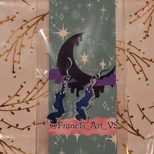 May include: A pair of blue and purple earrings shaped like a dripping, melting shape. The earrings are on a card with a crescent moon and stars. The card has the text "@Francis_Art_VS".
